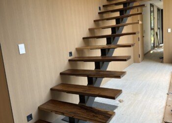 Escalera flotante a medida con estructura de herrería central y peldaños en madera maciza para obra residencial