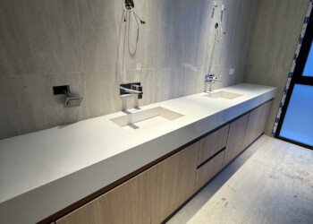 Vanitory suspendido en madera clara con bacha doble integrada en mesada blanca para baño principal