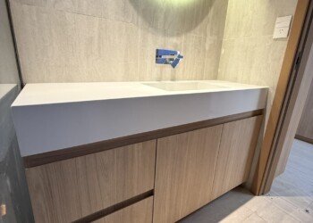 Mobiliario a medida para baño principal combinando madera clara, marmolería blanca y grifería de pared